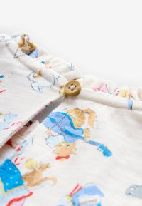 Lähedalt vaadatuna kangas, millel on värviline loomade ja mustrite trükk, millel on väike pruun nööp ja kogutud elastne serv.