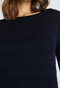 Maglione a maglia blu navy con strisce orizzontali testurizzate e una scollatura ampia, maniche lunghe e una leggermente aderente.