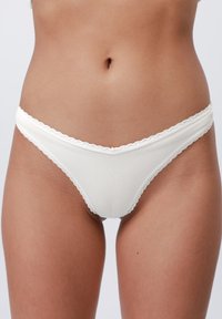 Witte geribbelde stringonderbroek met gegolfde randen, met een zachte textuur en een minimalistisch ontwerp.