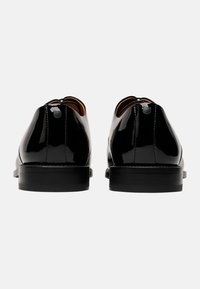 Scarpe in vernice nera con una finitura liscia, punta arrotondata, piccolo dettaglio a cerchio nella parte superiore e tacco in gomma nera.