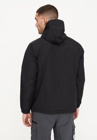 Schwarze leichte Jacke mit Kapuze, elastischen Bündchen und schlichtem Design, über grauen Hosen getragen, von hinten betrachtet.