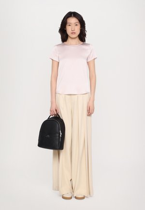 Zaino in pelle nera con forma arrotondata e manico superiore, abbinato a un top in satin rosa chiaro e pantaloni ampi plissettati beige.
