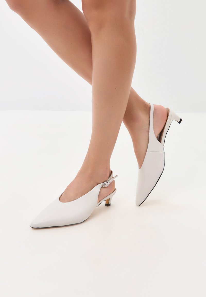 Décolleté bianchi con punta affusolata, caratterizzati da un design elegante, tacco sottile e accessori in argento. Materiale superiore liscio e suola a contrasto.
