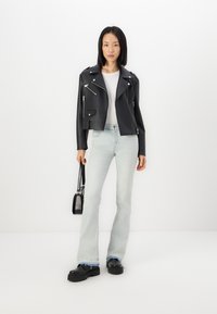 Veste de moto en cuir noir avec poches zippées, t-shirt blanc, jeans évasés bleu clair et chaussures à plateforme noires.