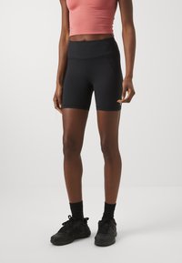 Pantaloni corti neri a vita alta con una texture liscia e un design elegante, abbinati a un top rosa aderente e scarpe da ginnastica nere.
