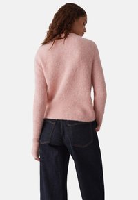 Pull en laine rose avec une texture douce et un design côtelé, porté avec un jean en denim foncé. Le pull a une coupe décontractée et des manches longues.