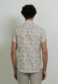 Camisa de manga corta con una tela ligera que presenta un suave patrón circular abstracto en tonos beige, marrón y blanco apagados.