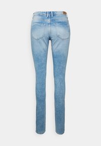 Jeans de denim azul claro com um corte justo, apresentando cinco bolsos, desbotamento subtil e um remendo de couro castanho na parte de trás da cintura.