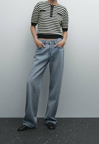 Randig svart och vit kortärmad topp med treknapps knäppning, i kombination med ljusblå vida jeans och svarta skor.