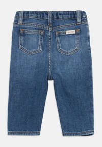Džinsai vidutinio mėlynumo spalvos, su elastinga juosta, dviem užpakalinėmis kišenėmis ir Calvin Klein logotipu ant užpakalinės kišenės.