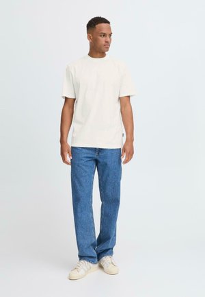 Camiseta de algodón crema con mangas cortas combinada con jeans de mezclilla azules y zapatillas off-white. Diseño simple con un ajuste relajado.