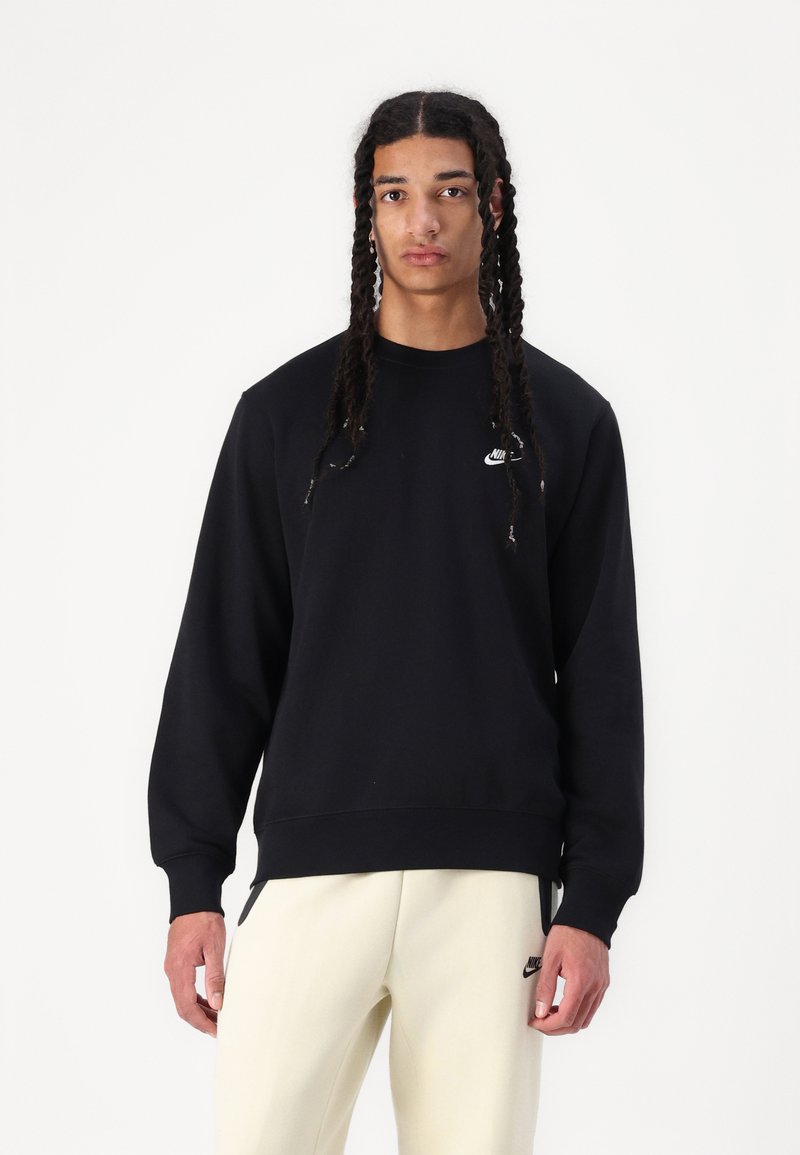 Svart genser med rund hals og lange ermer, med en liten hvit Nike-logo på brystet og ribbestrikkede mansjetter og kant.