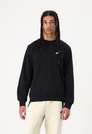 Black sweatshirt made of cotton blend, featuring a round neckline, ribbed cuffs, and a small white logo on the chest. Smooth texture.