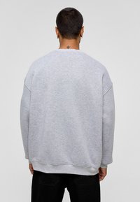 Grijze sweatshirt, oversized pasvorm, ronde halslijn, ribgebreide mouwen en zoom, zachte textuur, minimale details, gedragen over zwarte broek.