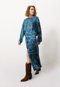 Türkisfarbener Zweiteiler mit abstrakten weißen Mustern; langärmliges Top und knöchellanger Rock, kombiniert mit beigefarbenen Wildleder-Cowboy-Stiefeln.