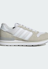 Baskets basses Adidas gris et blanc avec panneaux en mesh et en suède, lacets blancs, trois bandes blanches et semelle en caoutchouc.