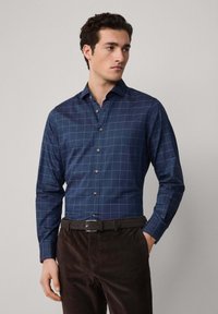 Marineblauwe overhemd met knoopjes, voorzien van een geruit patroon in wit en lichtblauw, gemaakt van een gladde stof, gecombineerd met donkerbruine corduroy broek.