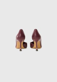 Burgundy leather high-heeled shoes with a rounded toe, open back, and a gold-accented heel. Smooth texture and sleek design.