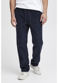 Tmavomodré manšestrové nohavice so šnúrkou v páse, s vertikálnou rebrovanou textúrou a voľným strihom, skombinované s bielymi teniskami.