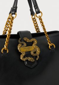 Zwarte leren handtas met gouden kettinghengsels, met een slangmotief en een plaatje waarop "JUST CAVALLI MILANO" staat. Gladde textuur.