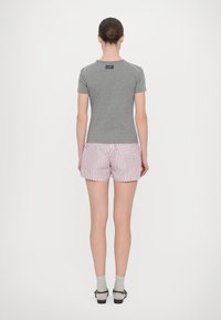 Camisa gris de manga corta con una etiqueta en la parte de atrás, combinada con pantalones cortos a rayas rojas y blancas. Medias y zapatos completan el conjunto.