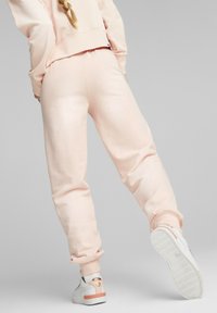 Pantalones jogger de color rosa claro con una textura suave y puños acanalados, combinados con zapatillas blancas que tienen un acento naranja en el talón.