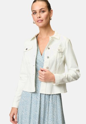 Veste en denim blanc au design ajusté, avec des boutons en argent et deux poches poitrine, associée à une robe bleue à motif floral.
