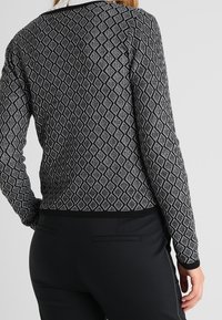 Svart och vit mönstrad stickad tröja med diamantdesign, långa ärmar och rund halsringning. Texturerad tyg med en solid svart nederkant.
