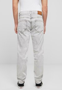 Heledad hall hallides denim püksid viie taskuga, seljaosal pruun nahkpatch ja veidi pleekinud tekstuur. Mustad tossud on nähtavad allpool.