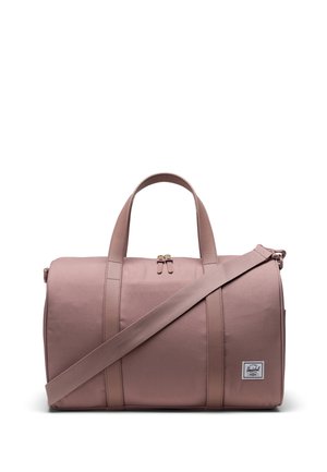 Sac de sport rose en tissu durable avec une forme arrondie, des poignées supérieures, une sangle adjustable, et un patch logo. Fermeture zippée et accents de couture.