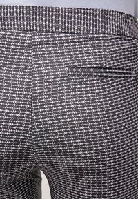 Svart och vitmönstrade korrekta byxor med ett bakfick och en ljusgrå skjorta instoppad i midjan.