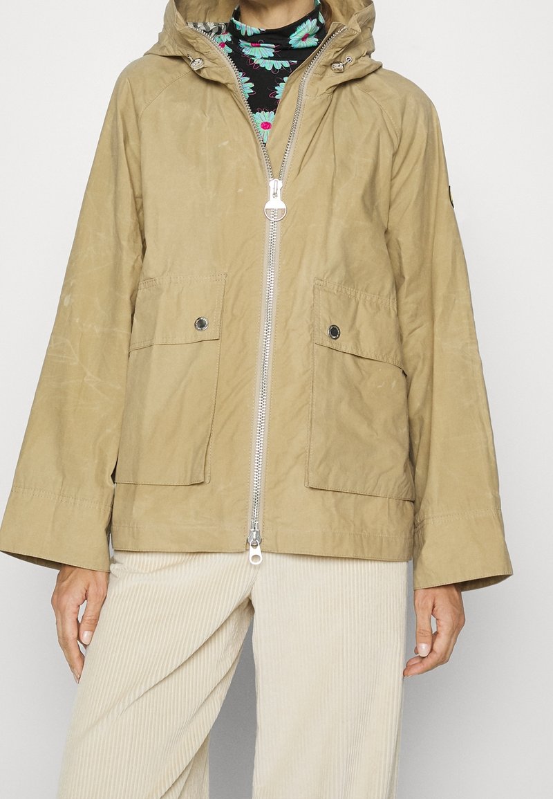Khaki lehká bunda s předním zipem, dvěma předními kapsami a nastavitelnou kapucí. Má hladkou, mírně texturovanou tkaninu.