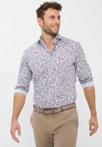 Weißes Hemd mit einem Blumenmuster in Blau und Braun, ausgestattet mit einem Button-Down-Kragen und hochgekrempelten Ärmeln. Kombiniert mit beigen Hosen.