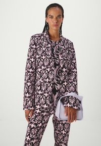 Pink and black patterned blazer and trousers set with leaf motifs, featuring a matching blouse and a light purple handbag. Smooth texture.
