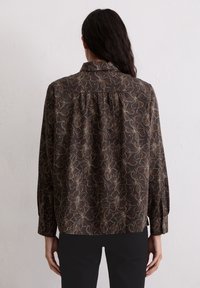 Ciemnobrązowa bluzka z kwiatowym wzorem w beżu i jasnoniebieskim. Posiada kołnierzyk, długie rękawy oraz plisę z tyłu zapewniającą większą swobodę ruchów.