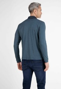 Langærmet teal polo med sort krave. Blød tekstur, lige kant, parret med mørkeblå jeans. Minimalistisk design og afslappet pasform.