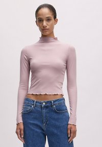 Helles rosa, geripptes Langarmoberteil mit hohem Kragen, verkürztem Design und gewelltem Saum, kombiniert mit hochgeschnittenen blauen Jeans.