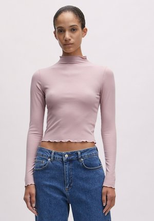 Helles rosa, geripptes Langarmoberteil mit hohem Kragen, verkürztem Design und gewelltem Saum, kombiniert mit hochgeschnittenen blauen Jeans.