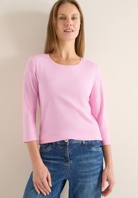 Haut à manches longues rose clair avec un col rond, en tissu lisse, associé à un jean en denim bleu. Design simple et ajusté.