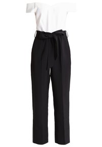 Haut blanc épaules dénudées associé à un pantalon noir taille haute avec une ceinture en tissu nouée à la taille.