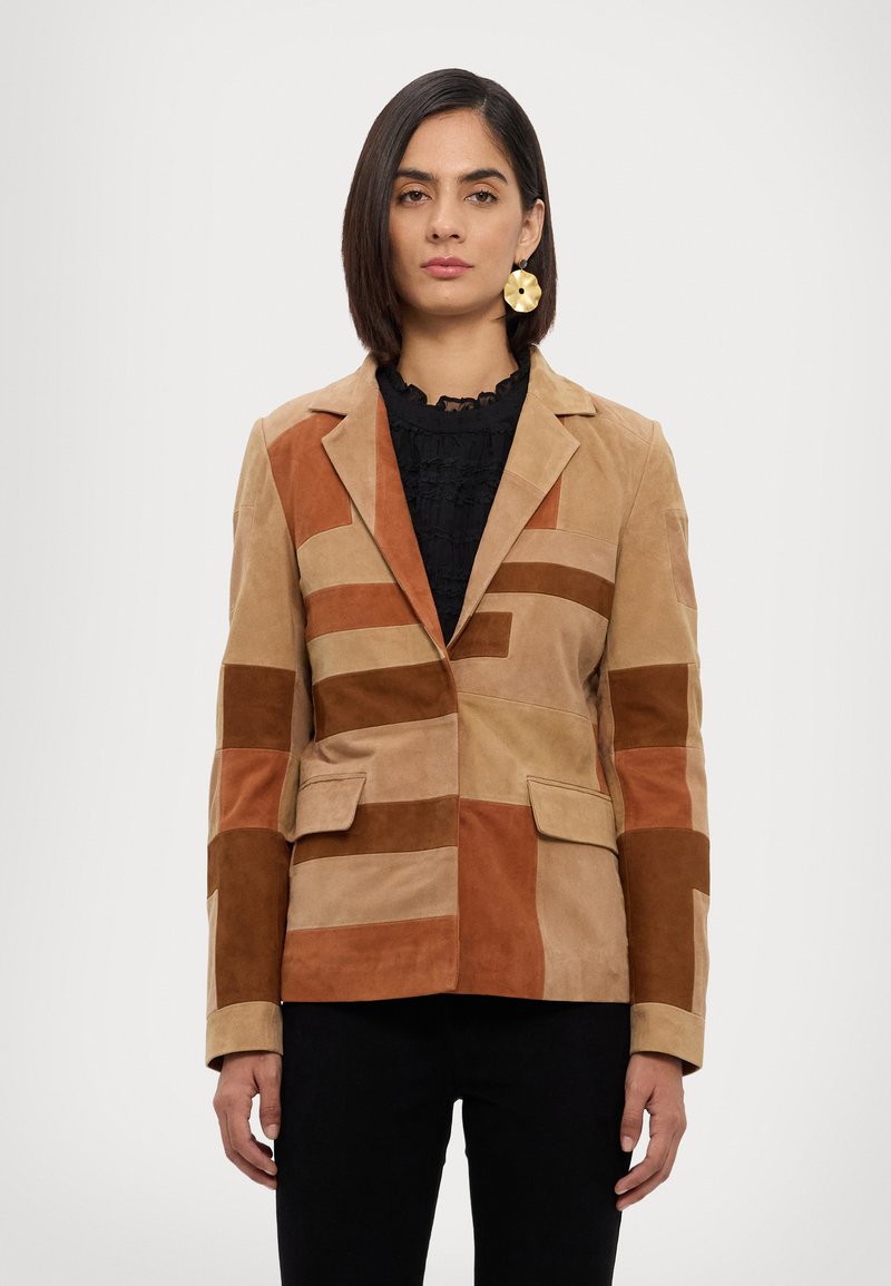 Blazer patchwork beige e marrone in suede, con colletto a scollo a V, due tasche frontali e rettangoli a contrasto in diverse tonalità.