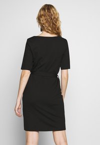 Czarna sukienka o dopasowanej sylwetce, z krótkimi rękawami i nieformalnym stylem. Posiada zwężoną talię z paskiem, co nadaje elegancki wygląd.