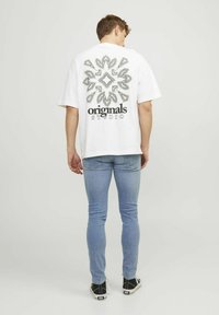 Tricou alb supradimensionat cu un grafic texturat alb-negru pe spate și cuvântul "originale" deasupra. Purtați cu blugi albaștri deschiși.