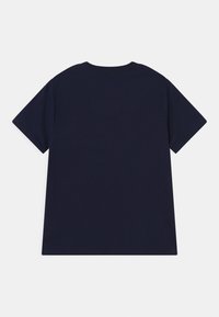 Námořnická modrá jednoduchá tričko s krátkým rukávem položené na stole, viděné zezadu, na bílém pozadí.