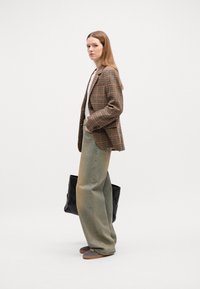 Blazer écossais brun sur un haut blanc, associé à un jean large bleu clair et des baskets grises. Sac fourre-tout tissé noir à la main.