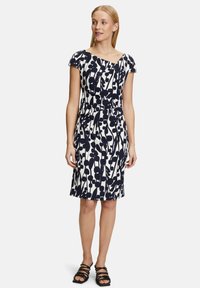 Robe blanche à manches courtes et longueur genou avec un motif floral bleu marine. Elle présente une taille cintrée et des détails froncés au niveau du col.