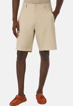 Shorts beiges en coton, dotés d'une fermeture à bouton, de poches latérales et d'une coupe droite, associés à des mocassins en suède orange.