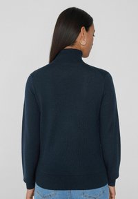 Suéter de punto azul marino con un cuello alto, puños y dobladillo acanalados. Diseño simple con una textura suave, visto desde la espalda.