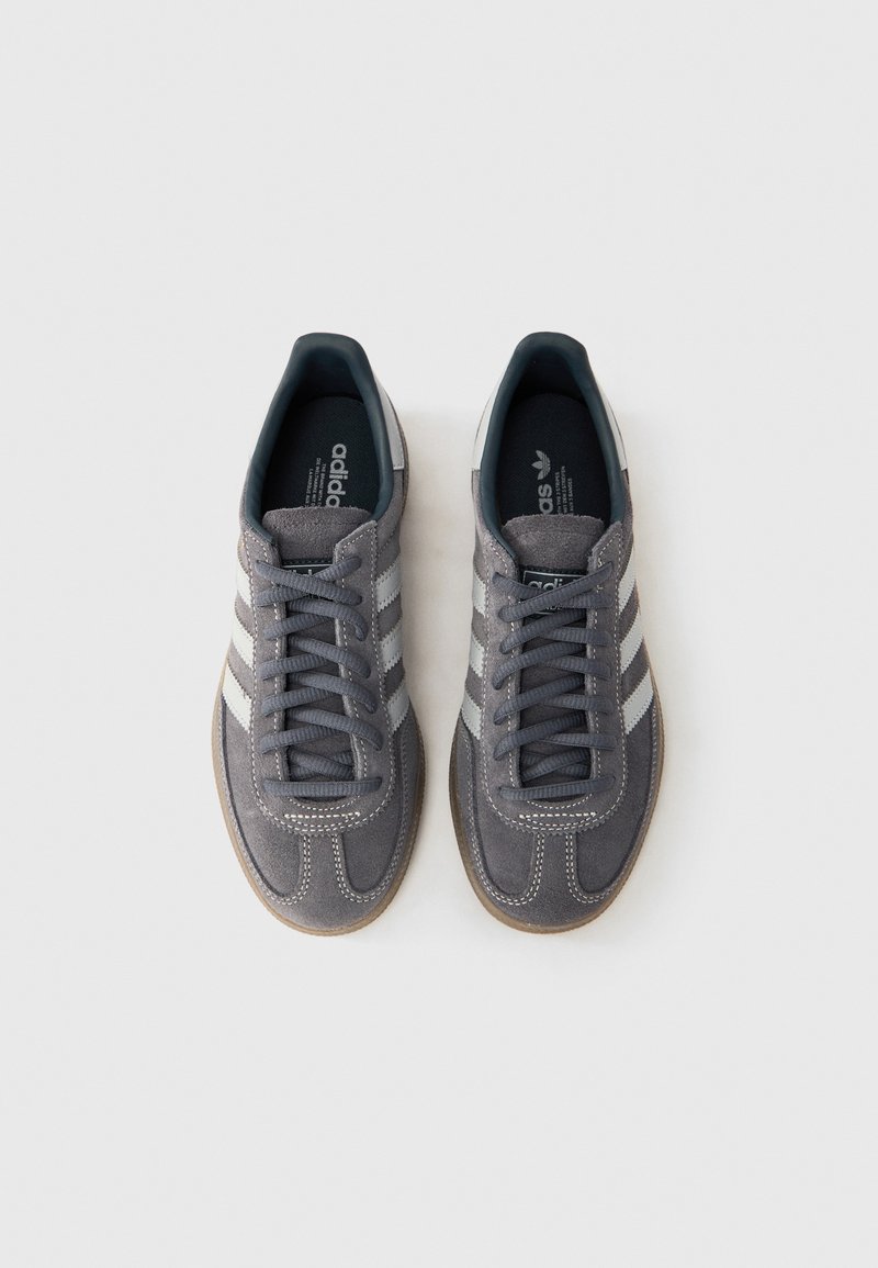 Gray suede sneakers with white stripes, round toe, and textured rubber sole. Displayed from above with laces and branding visible.