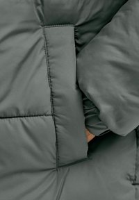 Mörkgrön vadderad jacka med quiltad struktur, sidoficka och ärmdetalj med samlad design och slät finish.